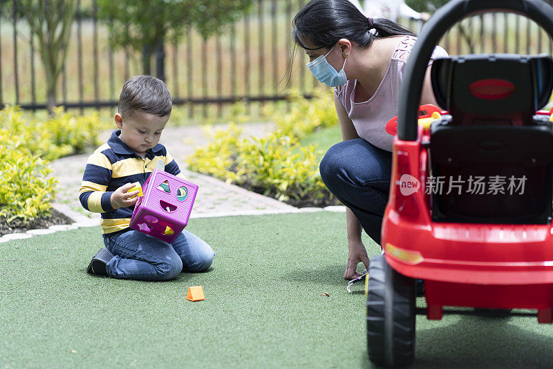 妈妈把他和他的孩子放在他的玩具车里，推着他带他出去散步，戴着他的防Covid - 19防护口罩